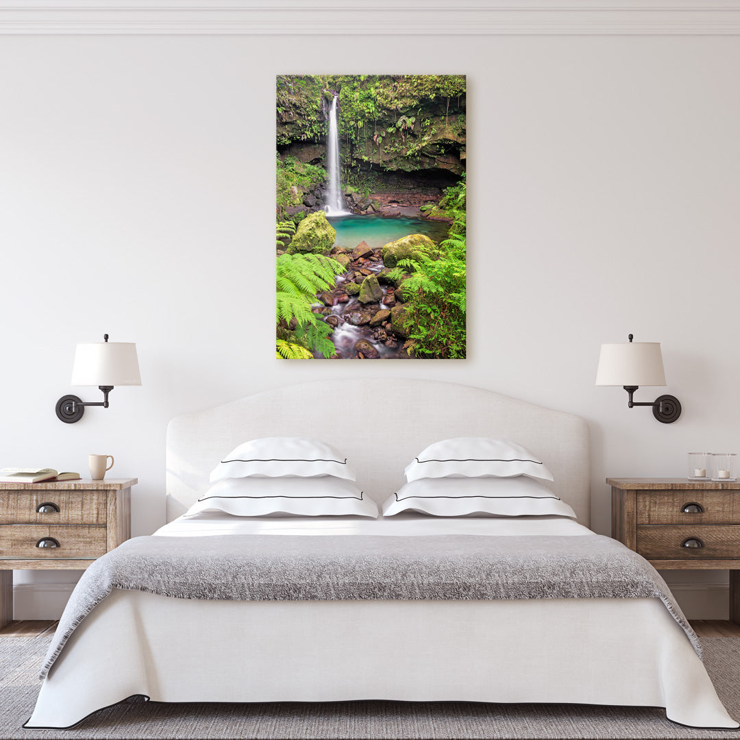 A canvas print of "Exquisite Emerald Pool" by Yuri A Jones on a light colored wall, hung above a queen sized bed with four pillows.