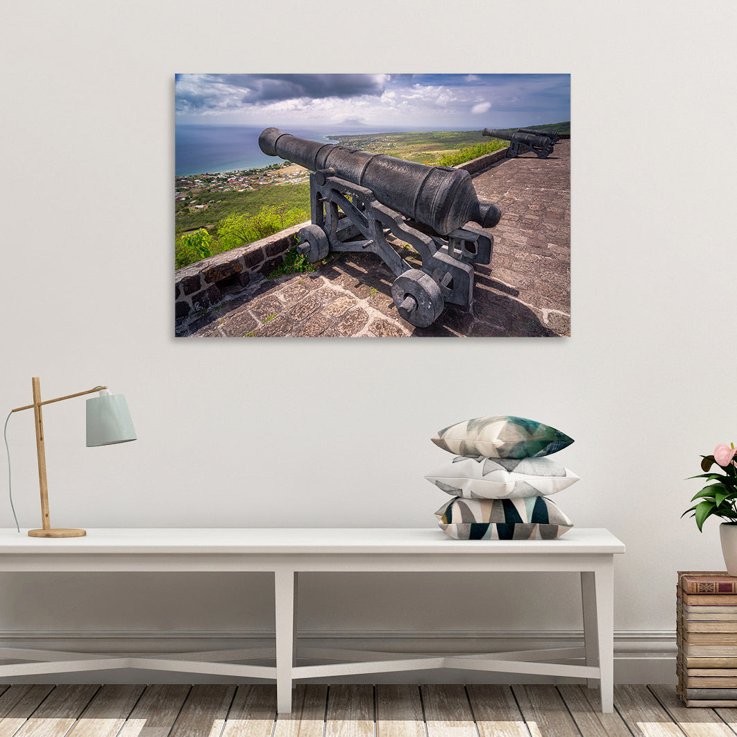 A canvas print of "Brimstone Hill Cannon II" by Yuri A Jones, on a white wall, hung above three cushions.