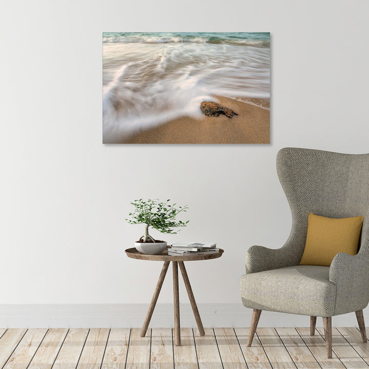 A canvas print of "Lover's Beach II" by Yuri A Jones on a white wall, hung above a brown striped armchair.