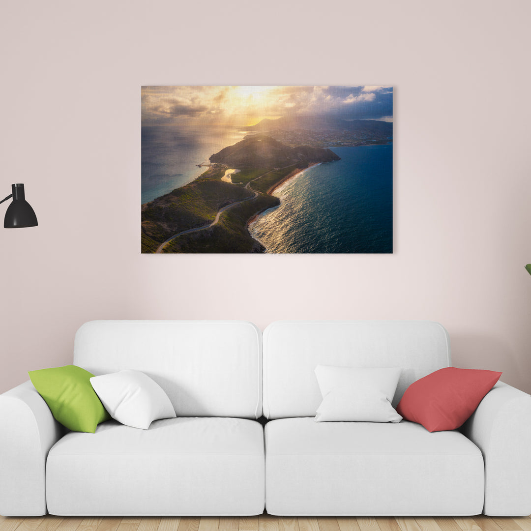 A canvas print of "Peninsula Sunset" by Yuri A Jones on a faded pink wall, hung above a white couch with four pillows.