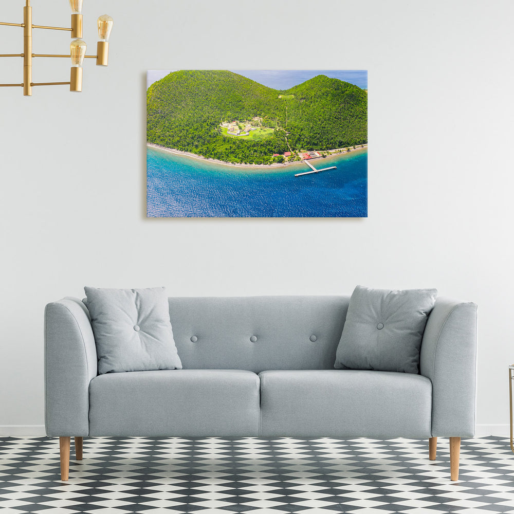 A canvas print of "Cabrits from Above I" by Yuri A Jones on a white wall, above a gray sofa.