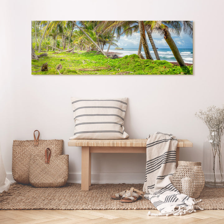 A canvas print of "Enchanted Cabana Beach" by Yuri A Jones on a light colored wall, above a bamboo bench with a striped throw-pillow.